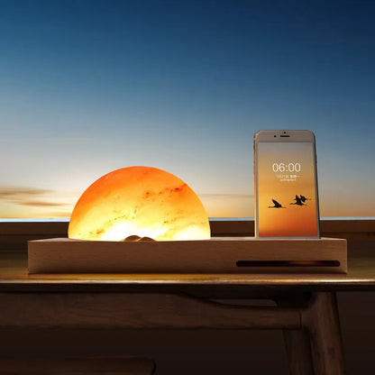 Natural crystal salt lamp with wooden base on a table, wirelessly charging a smartphone.