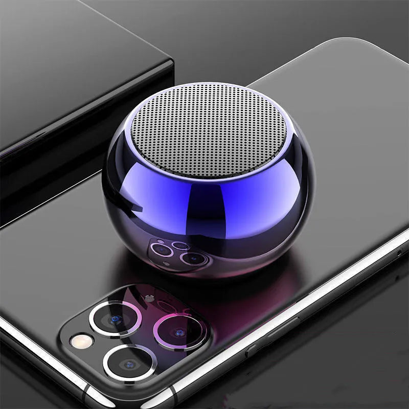 Small round aluminium Bluetooth speaker in gradient blue, showing compact size next to a USB cable.