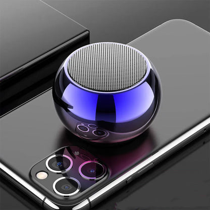 Small round aluminium Bluetooth speaker in gradient blue, showing compact size next to a USB cable.