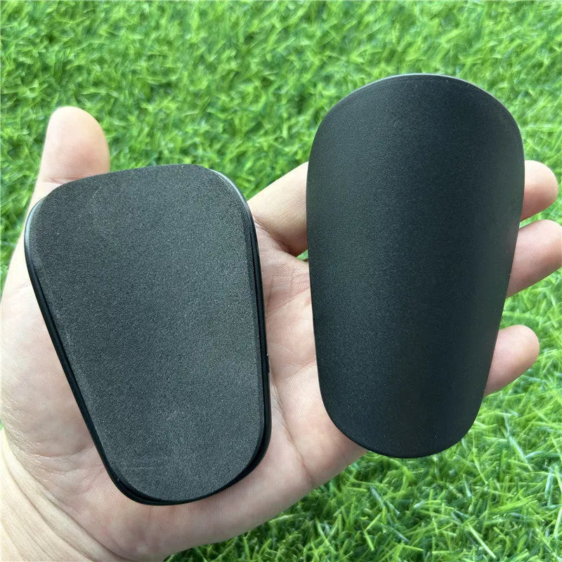 Extra small 8x5cm black and white plastic football shin guards for junior players.