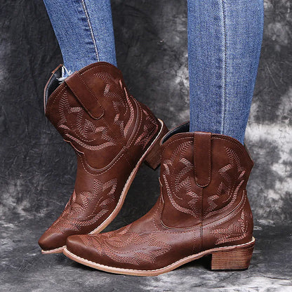 Blue women's cowboy ankle boots with embroidery and a low wedge heel on a wooden floor.