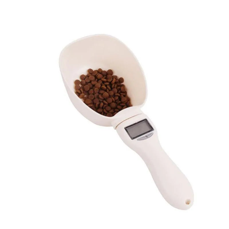 White electronic pet feeding weighing spoon with digital display and removable metal shovel head on a table.