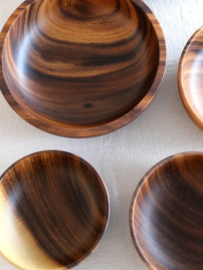 Set of five brown wooden bowls in different sizes on a wooden table, showing natural grain.