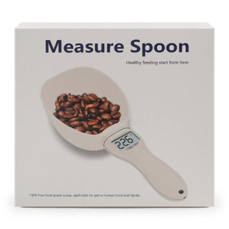 White electronic pet feeding weighing spoon with digital display and removable metal shovel head on a table.