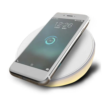 White wireless charging pad with digital clock display and three control buttons on a bedside table.