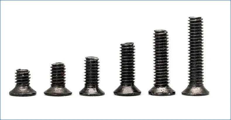 Black laptop machine screws with countersunk cross heads, shown in loose pile and close-up