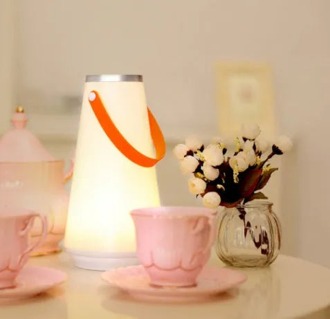White rechargeable LED lantern with USB cable on a bedside table.