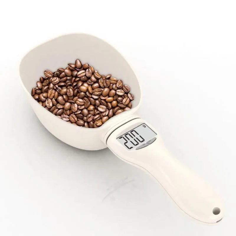 White electronic pet feeding weighing spoon with digital display and removable metal shovel head on a table.