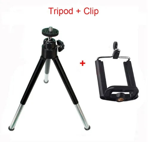 Black mini camera tripod with extended legs and a separate U-shaped universal phone clip on a table.