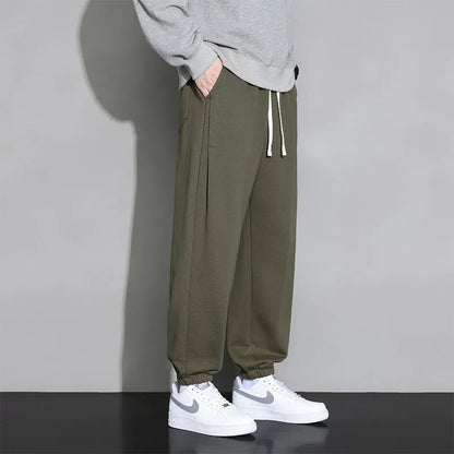 Man wearing loose grey sports trousers with an elasticated drawstring waistband.