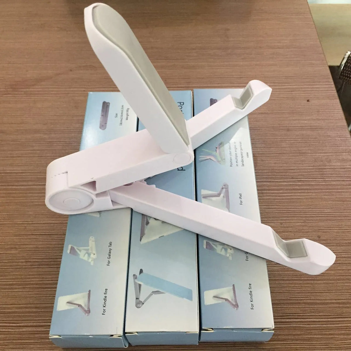 Black foldable tablet holder open in landscape mode holding a tablet, showing side buttons and non-slip base.