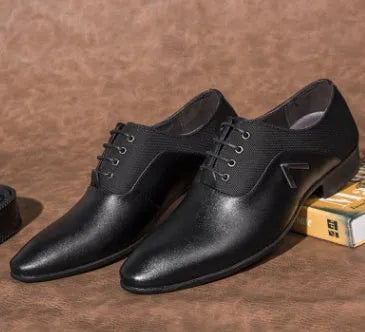 Men's black Oxford dress shoes with a rubber sole on a wooden floor.