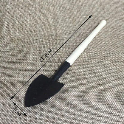 Succulent gardening tool set showing mini shovel, watering can, tweezers, and rake on a table.