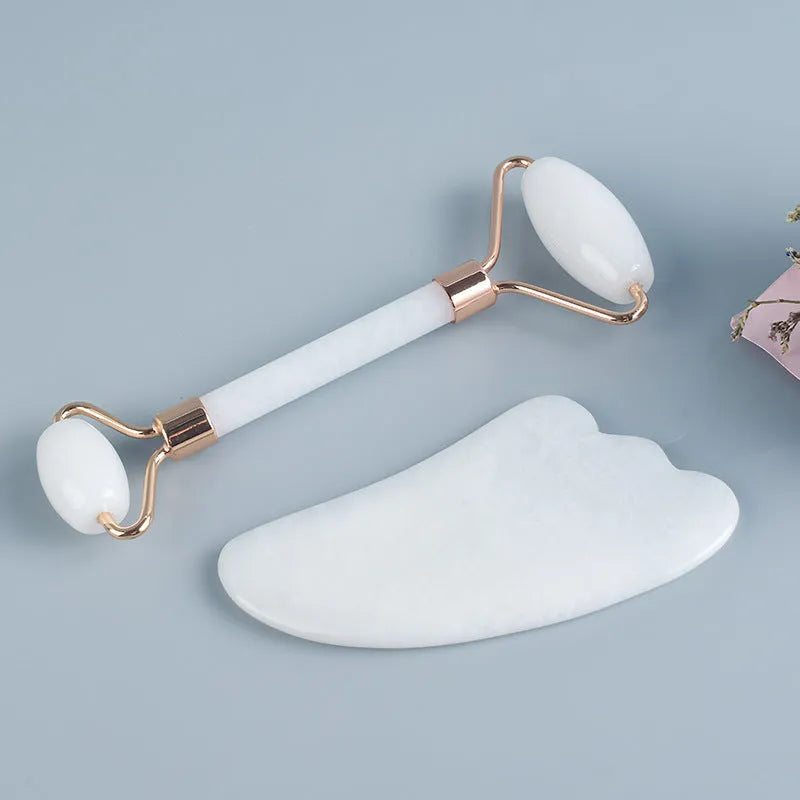 White jade facial roller with double-headed claw design and matching scraping board on dark surface