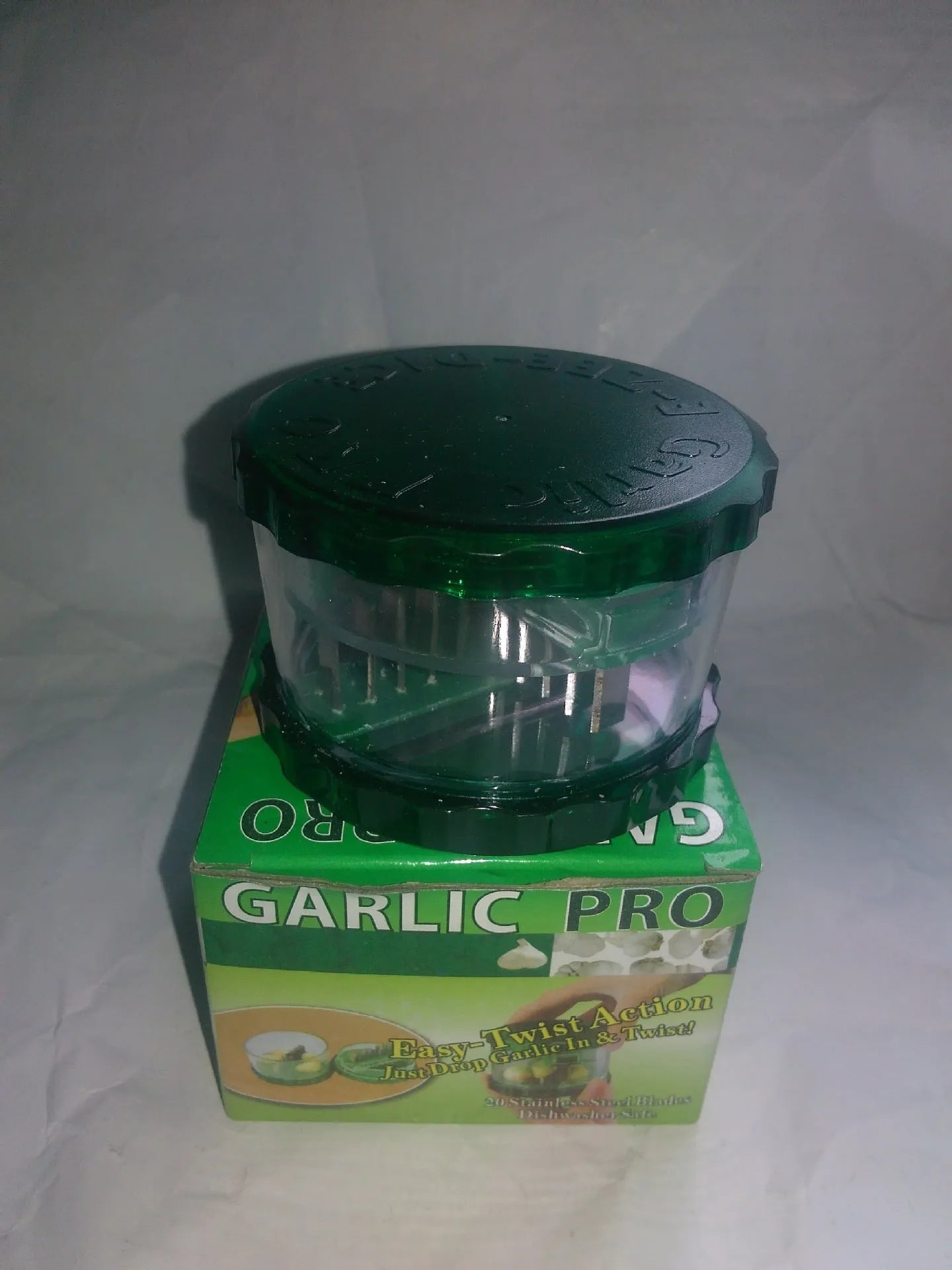 Transparent green garlic peeler measuring 8.5 by 8.5 by 6 centimetres with garlic cloves visible inside
