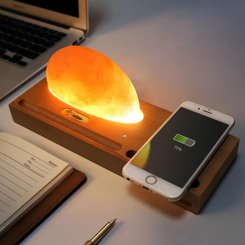 Natural crystal salt lamp with wooden base on a table, wirelessly charging a smartphone.