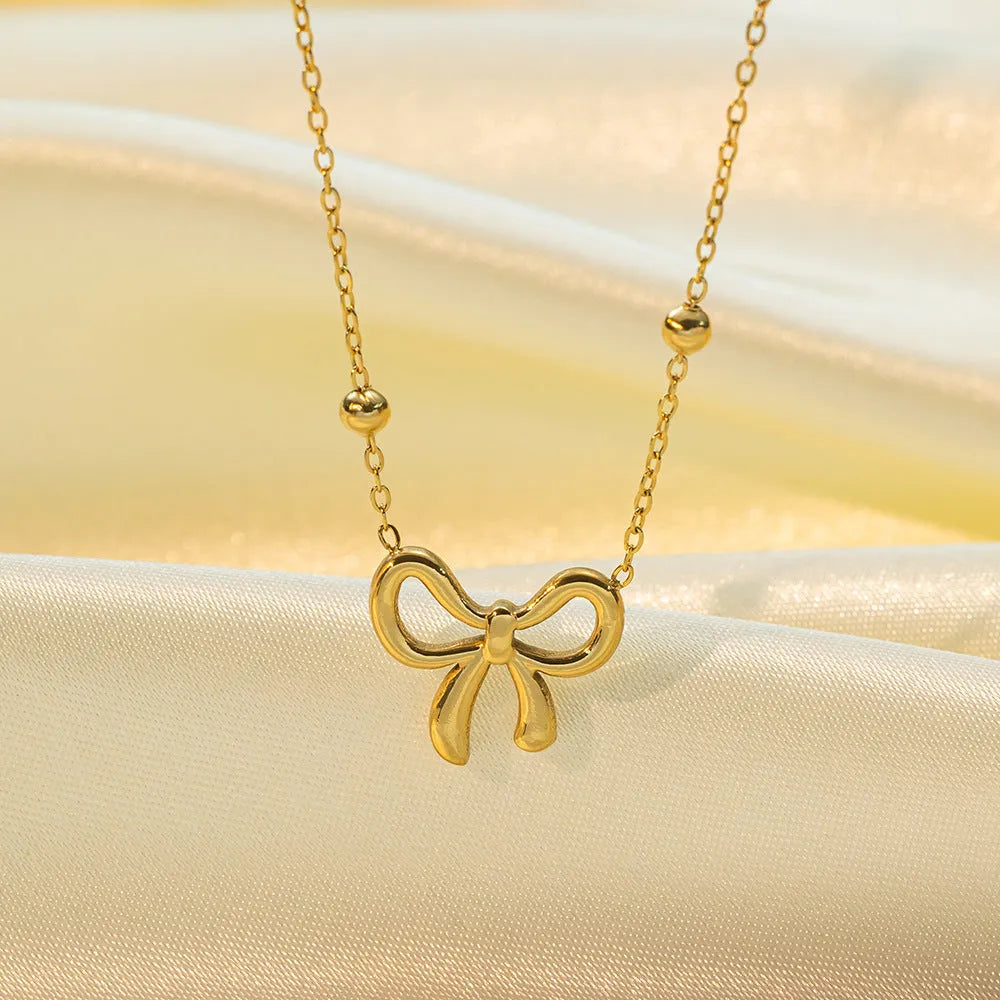 Gold adjustable bow necklace on a cross-link chain, showing the detailed pendant and clasp.