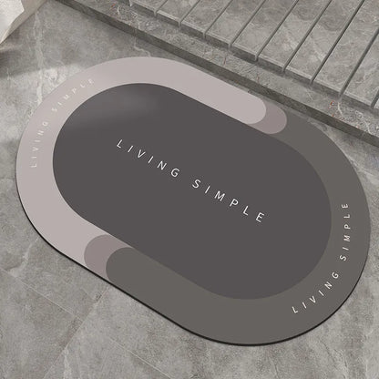 Oval grey bath mat with non-slip rubber bottom on a tiled floor, showing absorbent fabric surface