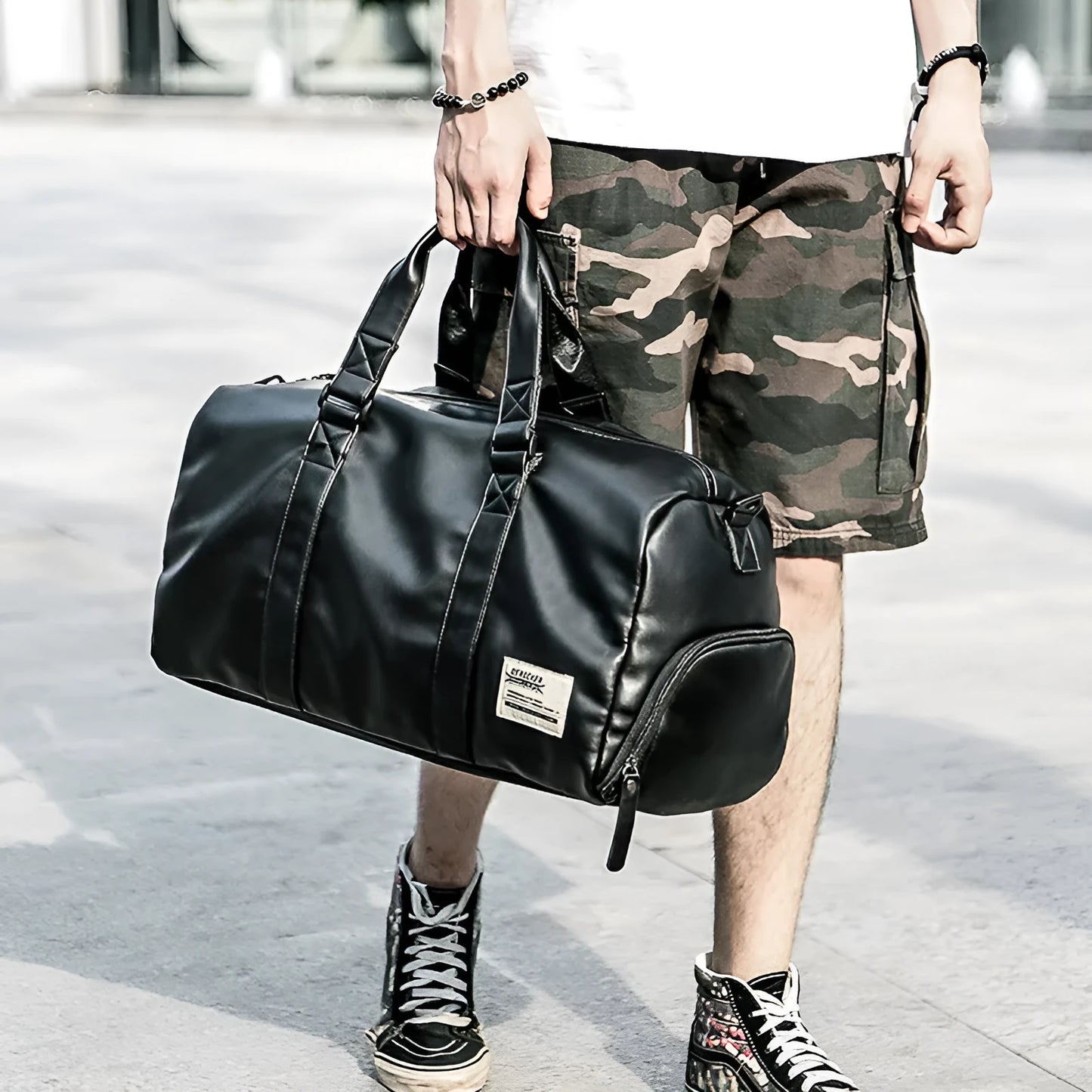 Large black waterproof PU leather sports duffel bag with multiple pockets, shown with a laptop and camera stored in its padded compartments.