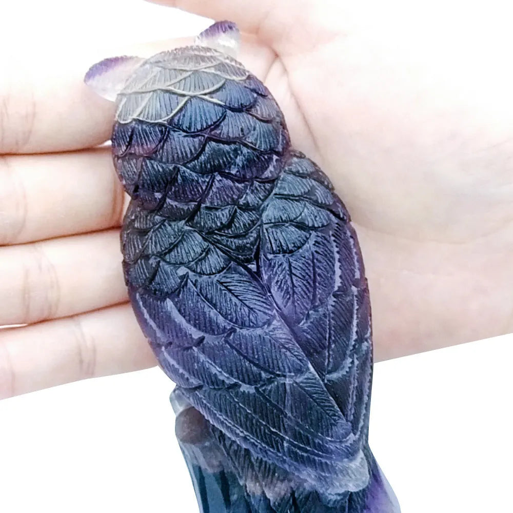 Hand-carved purple fluorite owl ornament on a neutral background, showing detailed carving and natural stone colour.