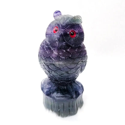Hand-carved purple fluorite owl ornament on a neutral background, showing detailed carving and natural stone colour.