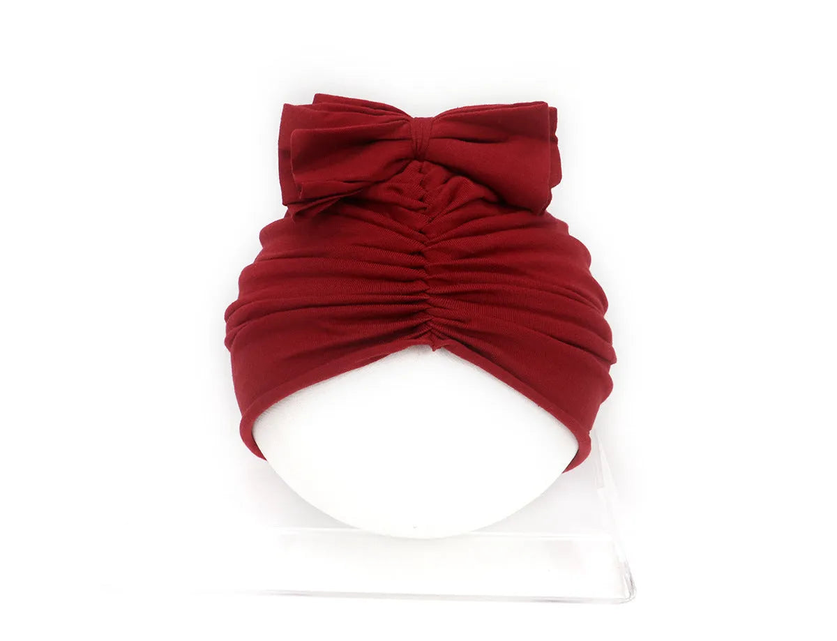 Soft acrylic knitted baby girl hat in a solid colour, shown fitting an infant.