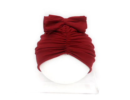 Soft acrylic knitted baby girl hat in a solid colour, shown fitting an infant.