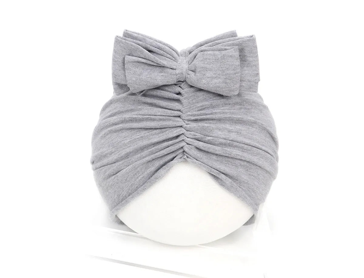 Soft acrylic knitted baby girl hat in a solid colour, shown fitting an infant.