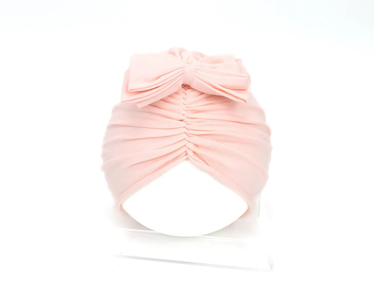 Soft acrylic knitted baby girl hat in a solid colour, shown fitting an infant.