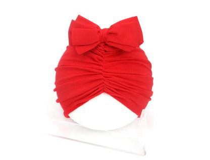 Soft acrylic knitted baby girl hat in a solid colour, shown fitting an infant.