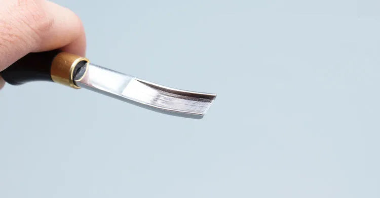 A leather-handled drum shovel wide shovel edge thinning knife on a workbench.