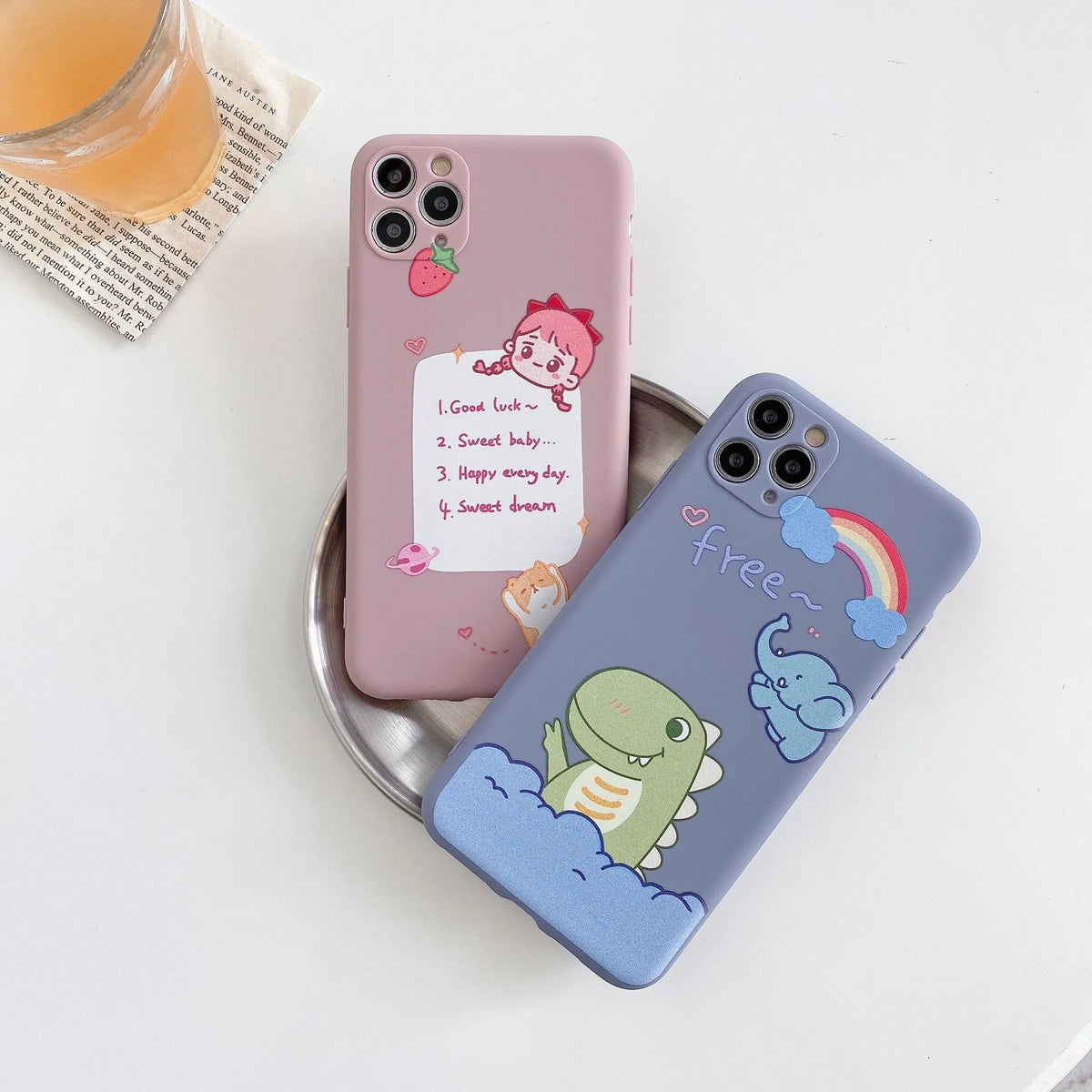 Blue frosted TPU iPhone case with a cartoon dinosaur print next to a pink case with a cat girl print.
