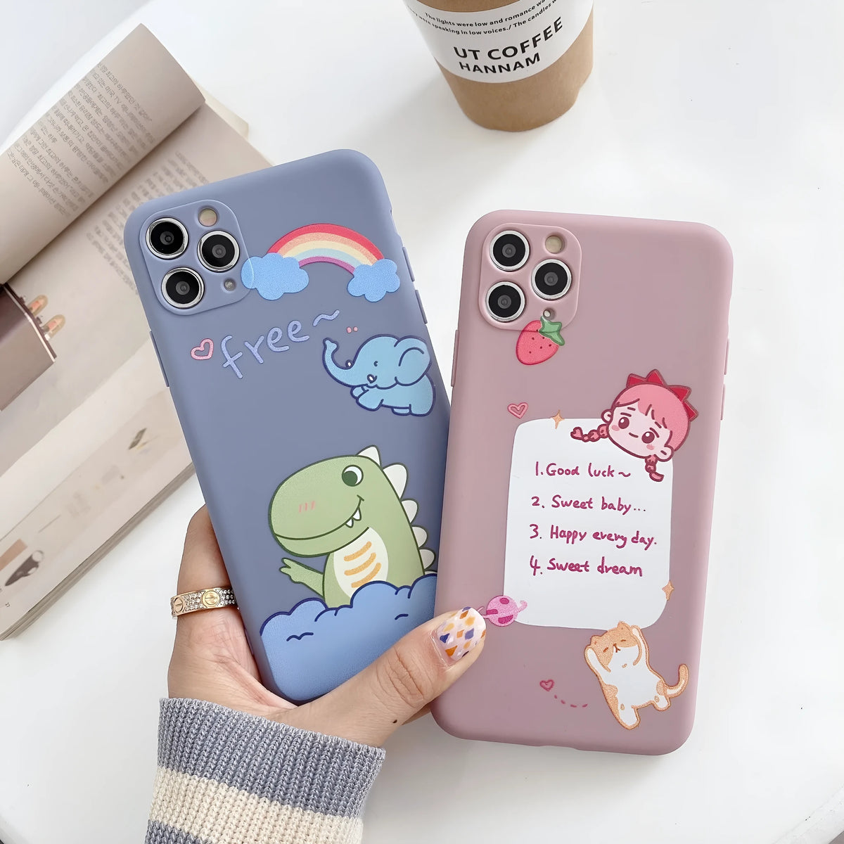 Blue frosted TPU iPhone case with a cartoon dinosaur print next to a pink case with a cat girl print.
