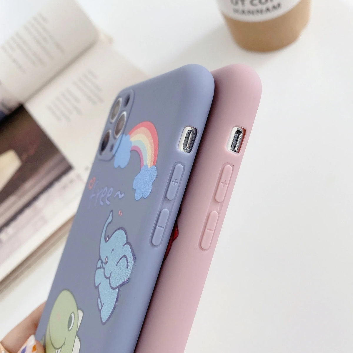 Blue frosted TPU iPhone case with a cartoon dinosaur print next to a pink case with a cat girl print.