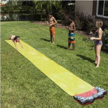 Children playing on a yellow inflatable water slide in a backyard garden