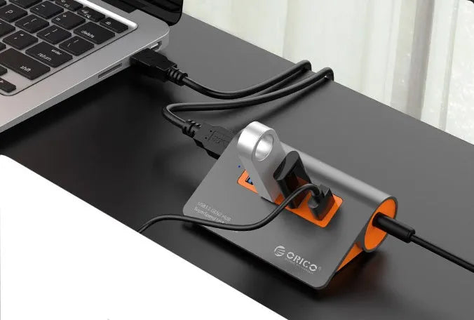 Dark grey and orange aluminium laptop hub with four USB ports, a blue LED light, and a detached cable.