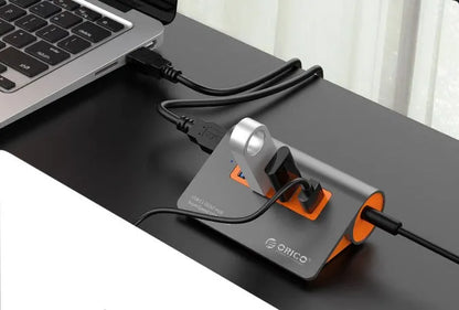 Dark grey and orange aluminium laptop hub with four USB ports, a blue LED light, and a detached cable.