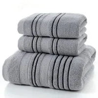Household pure cotton towel set showing one large bath towel and two smaller hand towels in a neutral colour like grey or khaki.