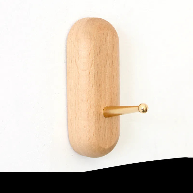 Natural beech wood adhesive wall hook in a capsule shape, shown on a wall for damage-free hanging.