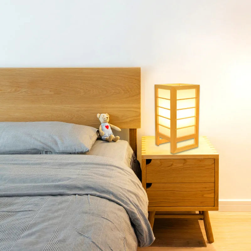 Minimalist solid bamboo wood bedside lamp with a tatami-inspired base and a fabric lamp shade on a wooden table.