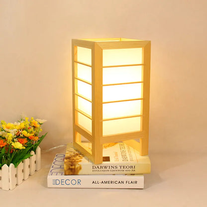 Minimalist solid bamboo wood bedside lamp with a tatami-inspired base and a fabric lamp shade on a wooden table.