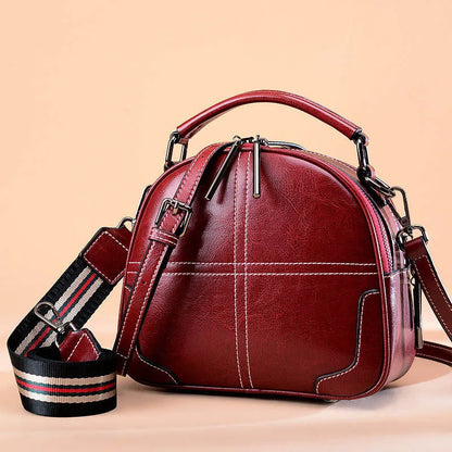 Round leather handbag with soft double handles and zipper closure in wine red colour