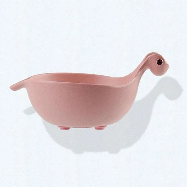Three colourful dinosaur-shaped bowls made from wheat straw in pink, green, and beige.