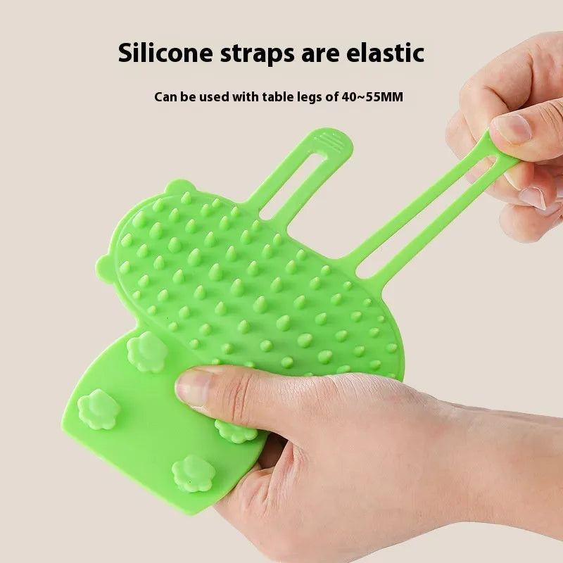 Silicone cat grooming comb with adjustable strap mounted on a table leg, shown in green.