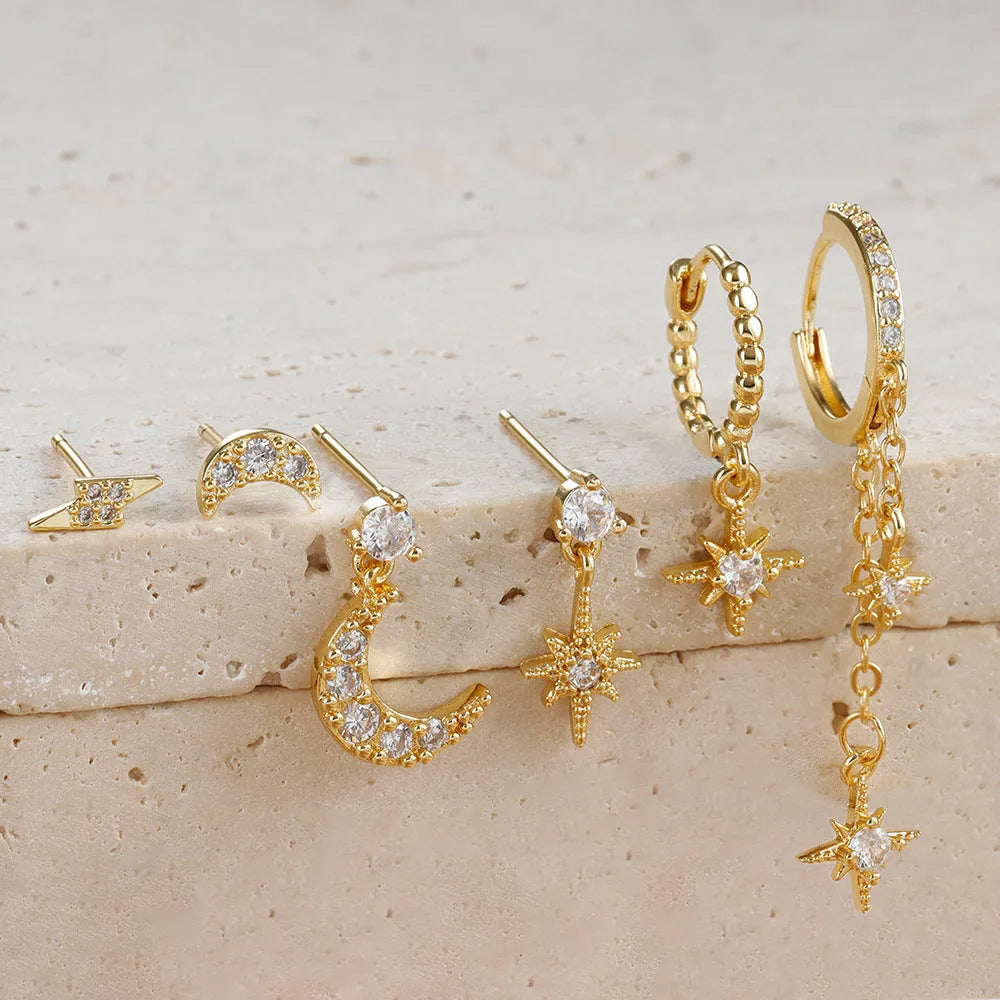Set of six gold-coloured XINGX chain tassel stud earrings with zircon details on a flat surface.