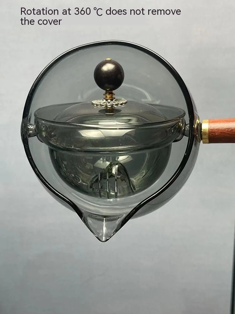 Transparent borosilicate glass rotary teapot with wooden handle and built-in infuser on a wooden surface