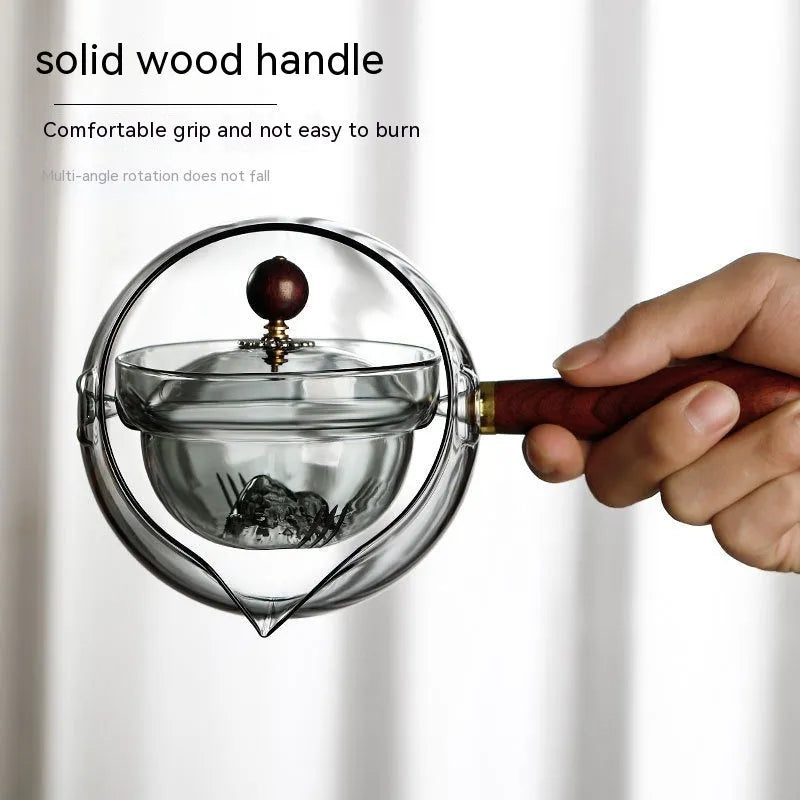 Transparent borosilicate glass rotary teapot with wooden handle and built-in infuser on a wooden surface