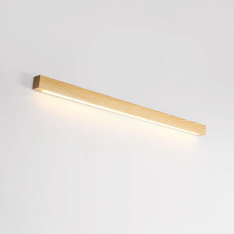 Slim walnut-coloured wooden strip wall lamp with acrylic light diffuser mounted on a plain wall.