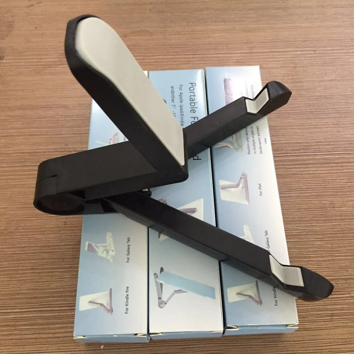 Black foldable tablet holder open in landscape mode holding a tablet, showing side buttons and non-slip base.