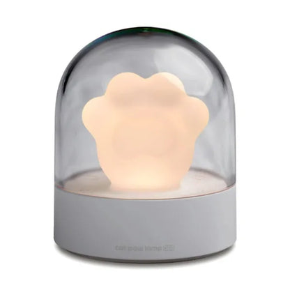Grey cat paw shaped night light with USB port, glowing softly on a wooden surface.